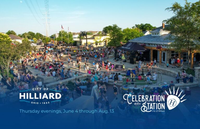 Outdoor community festival in a town square with a stage, seating on steps, and 'Celebration at the Station' banners nearby in Hilliard, Ohio.