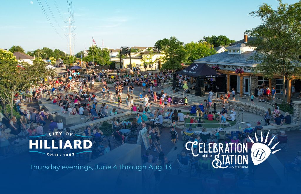 Outdoor community festival in a town square with a stage, seating on steps, and 'Celebration at the Station' banners nearby in Hilliard, Ohio.